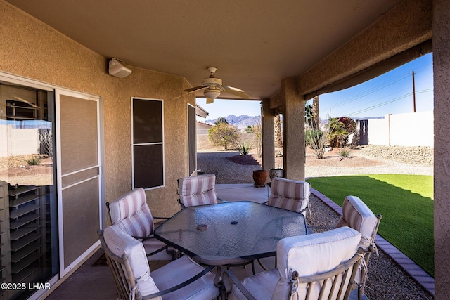 view of patio with a mountain view, outdoor dining area, fence, and a ceiling fan