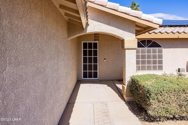 view of exterior entry with roof mounted solar panels, a tiled roof, and stucco siding