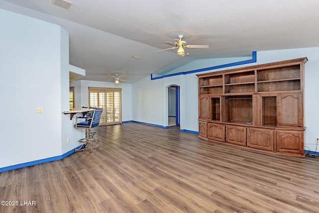 unfurnished living room featuring arched walkways, a ceiling fan, and wood finished floors