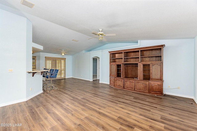 unfurnished living room with vaulted ceiling, wood finished floors, arched walkways, and ceiling fan