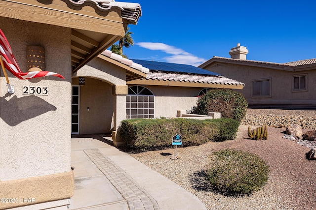 doorway to property with stucco siding, a tiled roof, and solar panels