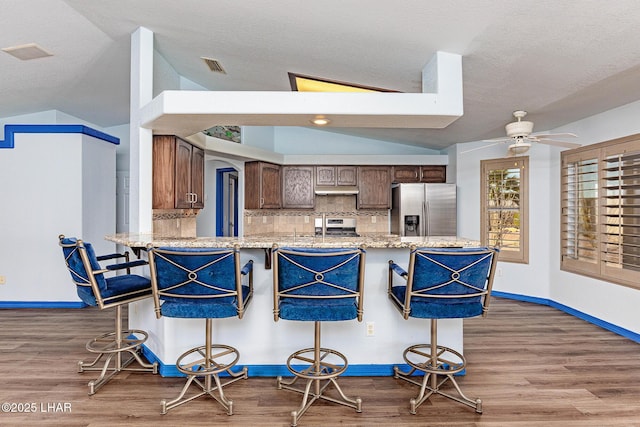 kitchen featuring lofted ceiling, visible vents, stainless steel refrigerator with ice dispenser, tasteful backsplash, and a kitchen bar