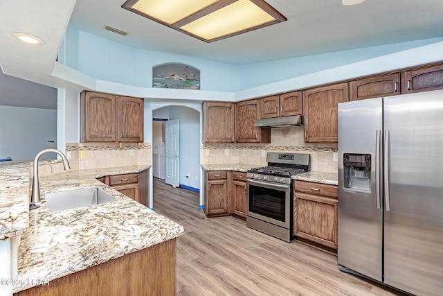 kitchen featuring arched walkways, stainless steel appliances, a sink, light wood-type flooring, and under cabinet range hood