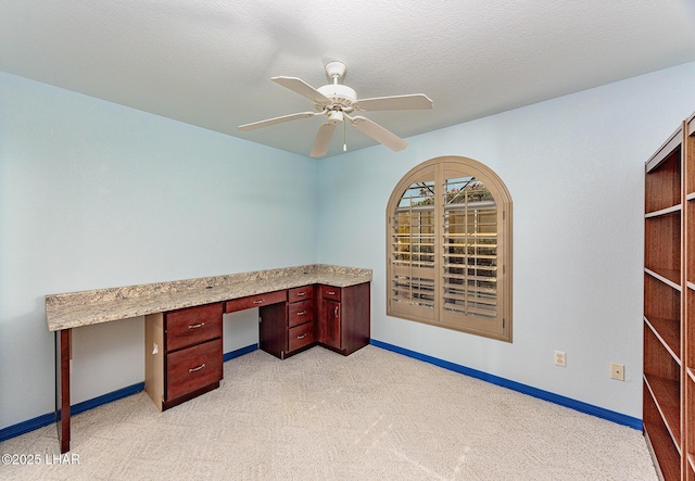 unfurnished office with ceiling fan, a textured ceiling, light carpet, baseboards, and built in desk