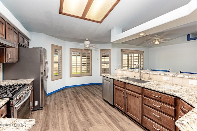 kitchen featuring stainless steel appliances, a sink, light stone countertops, and light wood-style floors