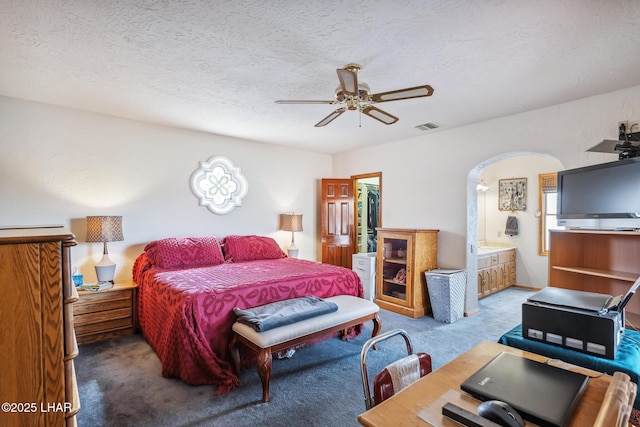 carpeted bedroom with arched walkways, visible vents, connected bathroom, ceiling fan, and a textured ceiling