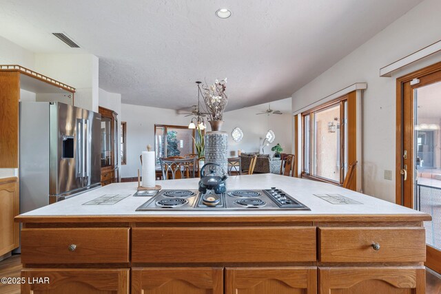 kitchen featuring a kitchen island, visible vents, light countertops, appliances with stainless steel finishes, and brown cabinets