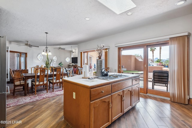 kitchen with a center island, a skylight, stainless steel cooktop, dark wood-type flooring, and a textured ceiling