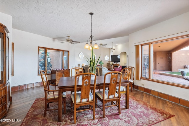 dining room with arched walkways, a textured ceiling, wood finished floors, baseboards, and ceiling fan with notable chandelier