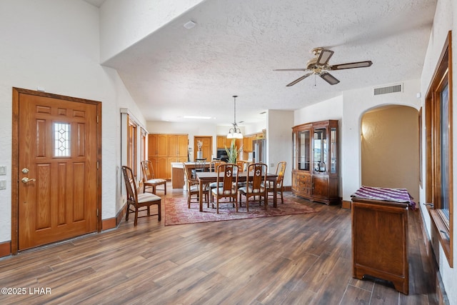 dining area featuring visible vents, arched walkways, ceiling fan, dark wood-type flooring, and a textured ceiling