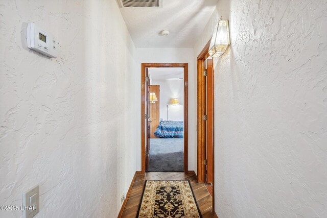 hallway with visible vents, wood finished floors, and a textured wall