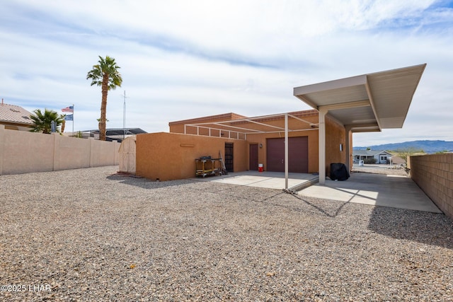 rear view of house featuring an attached garage, fence, and stucco siding