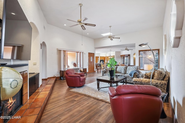 living room with arched walkways, recessed lighting, wood finished floors, a towering ceiling, and a tiled fireplace