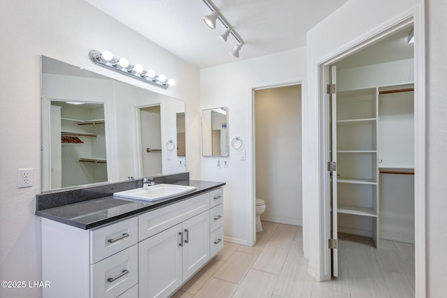 bathroom with track lighting, a walk in closet, vanity, and toilet