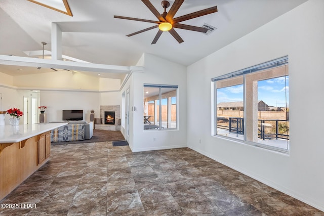 unfurnished living room featuring a warm lit fireplace, visible vents, baseboards, ceiling fan, and vaulted ceiling