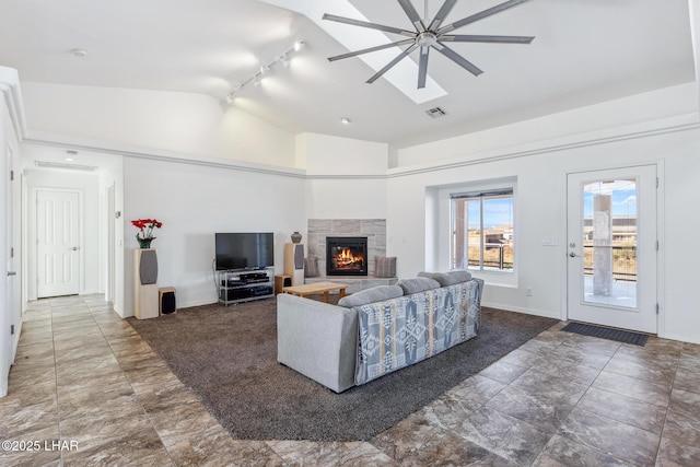 living area featuring a warm lit fireplace, visible vents, baseboards, ceiling fan, and vaulted ceiling