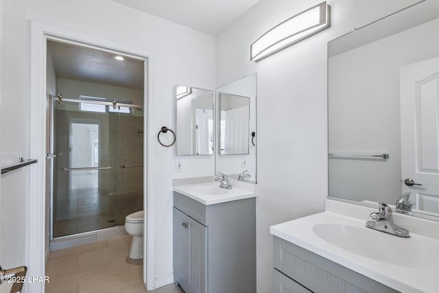 full bathroom featuring toilet, a shower stall, two vanities, and a sink