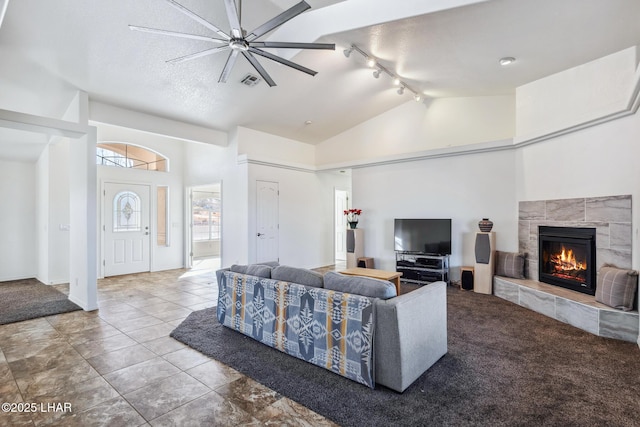 living area with a fireplace, rail lighting, a textured ceiling, high vaulted ceiling, and tile patterned floors