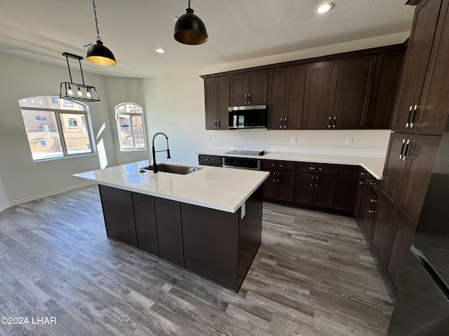 kitchen with sink, decorative light fixtures, dark brown cabinets, a center island with sink, and hardwood / wood-style floors