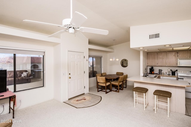 interior space featuring lofted ceiling, a breakfast bar area, light colored carpet, kitchen peninsula, and white appliances