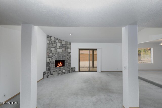 unfurnished living room featuring a stone fireplace, a textured ceiling, carpet floors, and a wealth of natural light