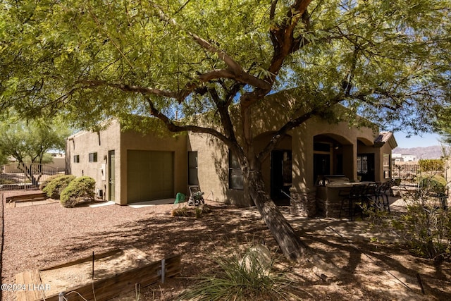 view of front of house featuring stucco siding, a patio, a garage, and fence