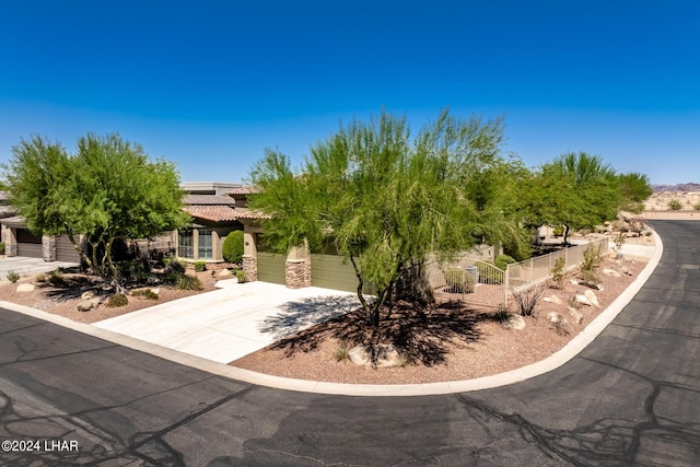 view of property hidden behind natural elements with fence, concrete driveway, stone siding, a tiled roof, and roof mounted solar panels