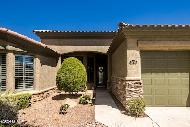 entrance to property featuring stucco siding, stone siding, and an attached garage