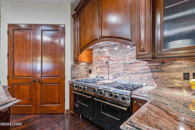 kitchen with dark stone countertops, decorative backsplash, dark wood-type flooring, and range with two ovens