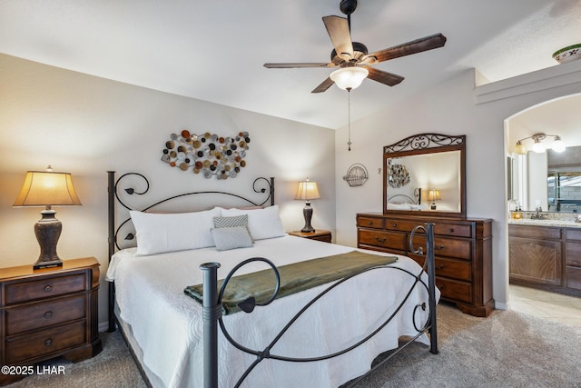 bedroom with a ceiling fan, arched walkways, vaulted ceiling, light colored carpet, and connected bathroom