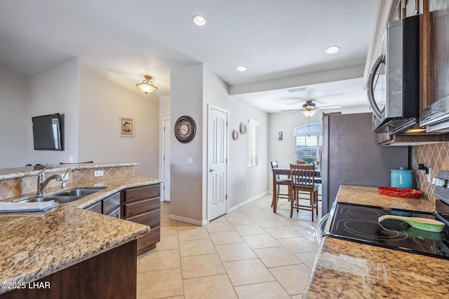 kitchen featuring a ceiling fan, a sink, backsplash, appliances with stainless steel finishes, and light tile patterned floors