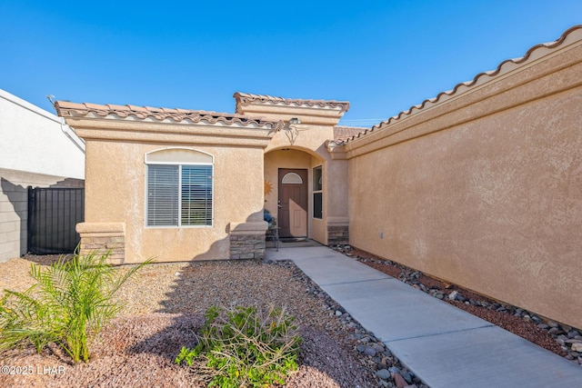 property entrance with stone siding, stucco siding, a tile roof, and fence