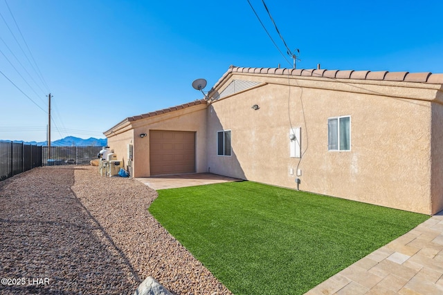 rear view of property with fence, stucco siding, a lawn, driveway, and an attached garage