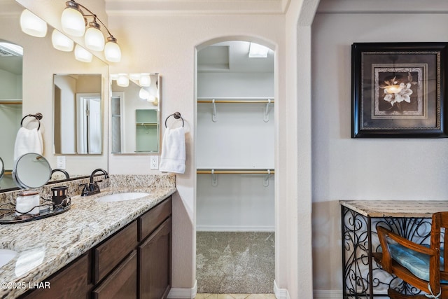 bathroom featuring double vanity, a spacious closet, baseboards, and a sink