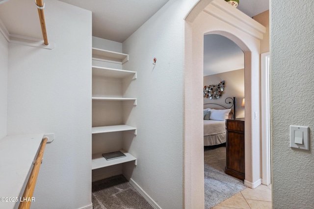 walk in closet with arched walkways and light tile patterned floors