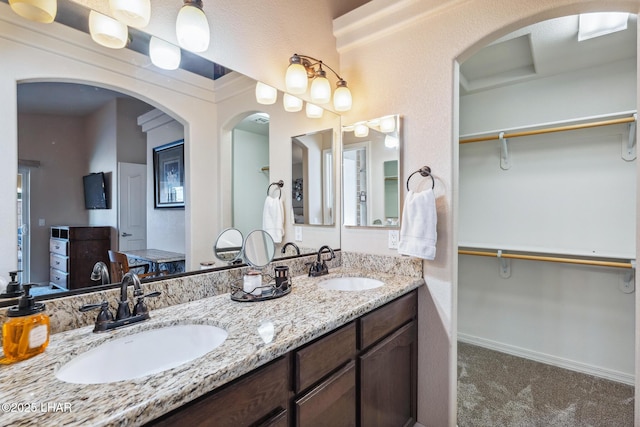 bathroom with a walk in closet, double vanity, baseboards, and a sink