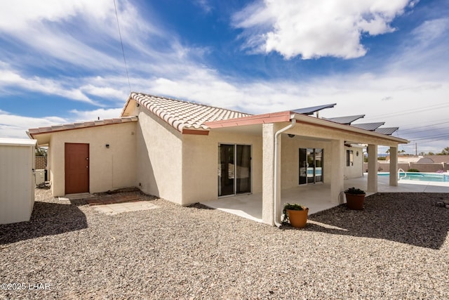 back of property featuring a fenced in pool, stucco siding, roof mounted solar panels, a patio area, and a tiled roof