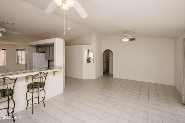 kitchen featuring tile countertops, ceiling fan, white refrigerator with ice dispenser, and arched walkways