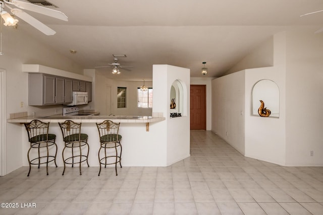 kitchen featuring lofted ceiling, white appliances, a kitchen bar, and a ceiling fan