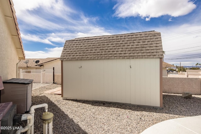 view of property exterior featuring a shed, mansard roof, roof with shingles, and fence