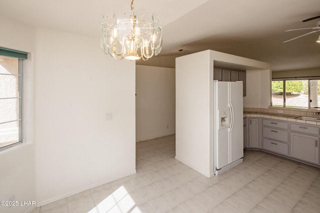 kitchen with hanging light fixtures, white fridge with ice dispenser, and ceiling fan with notable chandelier