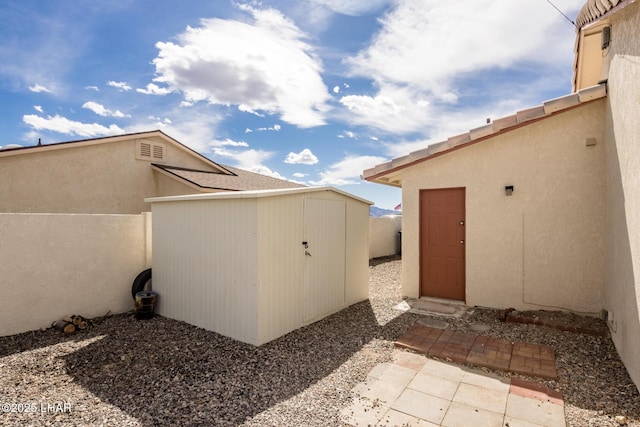 exterior space featuring an outbuilding, a storage unit, fence, and stucco siding