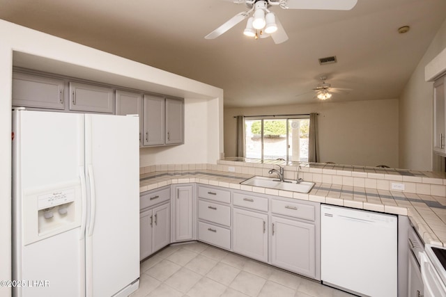 kitchen featuring tile countertops, ceiling fan, white appliances, a sink, and visible vents