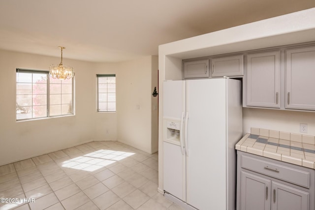 kitchen with white refrigerator with ice dispenser, decorative light fixtures, tile countertops, gray cabinetry, and an inviting chandelier