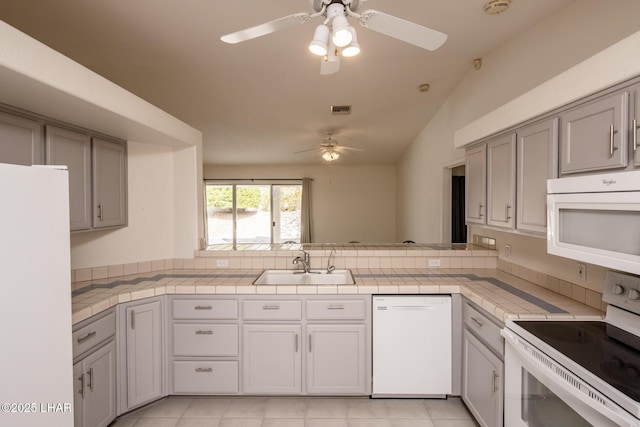 kitchen with tile counters, visible vents, a sink, white appliances, and a peninsula