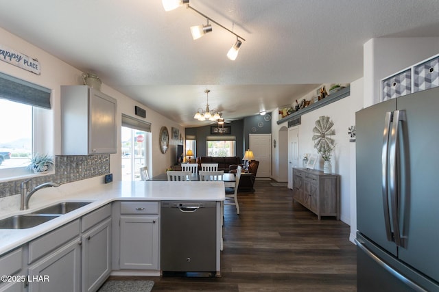 kitchen featuring a sink, appliances with stainless steel finishes, dark wood finished floors, a peninsula, and a notable chandelier
