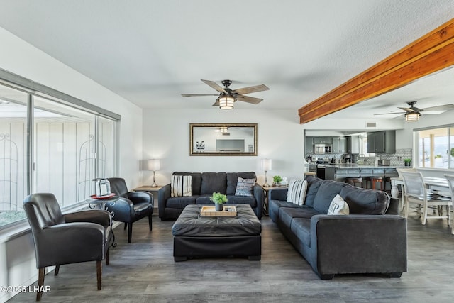 living area with ceiling fan, dark wood-style flooring, and beam ceiling