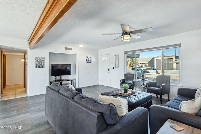 living area with a textured ceiling, ceiling fan, visible vents, beam ceiling, and dark wood finished floors