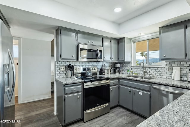 kitchen with light stone counters, dark wood finished floors, stainless steel appliances, gray cabinets, and a sink