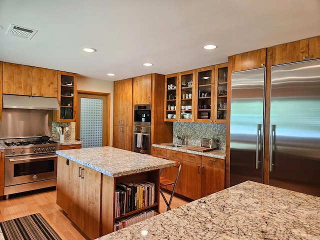 kitchen with light stone counters, a center island, light hardwood / wood-style flooring, premium appliances, and backsplash